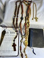 Photo showing two religious books laid open with three wooden rosaries and one relic cross pendant with chain laid on a white cloth.
