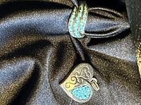 Photo displaying heart-shaped sterling silver pendant with turquoise inlay and decorative swirls.