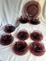 Full set of 8 amethyst purple Duralex Rivage glass cups and matching saucers displayed with the additional small plate behind them, showing the rippled swirl pattern.