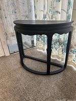 Front angle showing half round shape of hardwood entry table and scalloped apron with carved detailing.