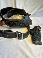 Photo showing the two black leather belts with embossed designs and the woven leather holster.