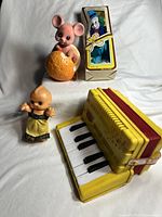 Four vintage items: yellow accordion, Kewpie doll, boxed clown figure, bobblehead mouse piggy bank on white surface
