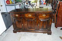 Buffet with closed drawers and cabinet doors in a dark wood finish with brass handles shown from the front.