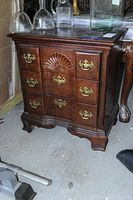 Front view of the solid wood side chest showing the carved shell detail and ornate brass handles on three drawers.