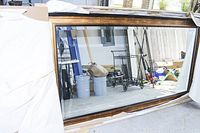 Wide view of the large wood-framed wall mirror crated and partially unpacked showing the full length and reflections of a garage interior.