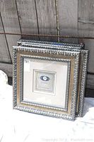 Four matching square silver decorative frames stacked and standing upright showing the ornate silver edging and beige mat.