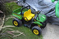 Three-quarter view of green and yellow two-seat ride-on vehicle on grass