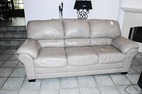 Front view of tan leather 3-seat sofa showing plush cushions and padded arms, placed on tile floor.