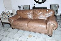Full view of the brown leather two-seat sofa with cushions and brass tacks visible