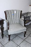 Front angled view of green upholstered arm chair with tufted channel back and cherry wood accents on arms and legs.