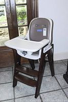 Full view of baby high chair with white plastic tray attached, dark wood frame and steps, gray leather seat and back.