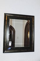 Full view of wall mirror with dark wide metallic frame and beveled glass hung on wall.