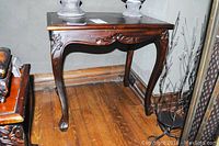 Side view of larger wooden end table showing carved front apron and cabriole legs with decorative carving and carved feet