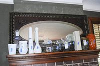 Wide view of the large mirror mounted above a mantel, showing its full size and frame details alongside decorative items on the mantel.