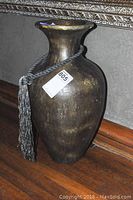 Front side view of the large vintage style vase showing its shape and decorative tassel.