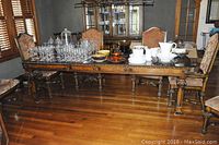 Full view of the large solid wood dining room table with carved legs and two leaves, surrounded by upholstered chairs.