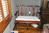 Full view of the wooden settee with upholstered seat, showing carved wooden details on back, arms, front, and legs.