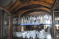 Glassware and serving pieces displayed on an upper cabinet shelf: large wine glasses, cake stand, cake server, candy dish, bowl, and butter dish