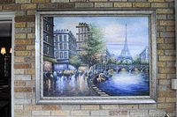 View of the full oil painting mounted on wall, showing Eiffel Tower, river scene, and decorative silver frame.