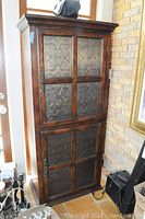 Front view of closed cabinet showing decorative metal panels on doors and crown molding top
