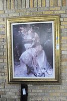Full view of the framed print hanging against a brick wall, showing the entire artwork and ornate gold frame.