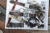 Overview of all items in the lot showing various men's watches and cuff links inside a white container.