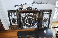 Three decorative metal items arranged together: a bronze and black ornate chimney screen with circular floral medallion flanked by two smaller matching side panels, and two other metal gates with vertical slats and arched tops.