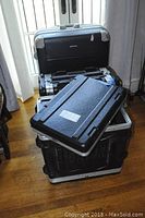 Photo showing the three items stacked: two large black rack cases and one rolling suitcase behind them