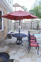 Red square outdoor patio umbrella fully opened, mounted on a black round metal patio table with matching chairs.