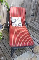 Front view of one metal chaise lounge with red and white striped cushion and floral pillow on wooden deck.