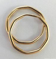 Two polygonal small hoop earrings placed together on a flat light surface showing their shape and clasp.