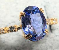 Close-up of oval tanzanite center stone and prong setting with diamond accents on band