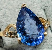 Close-up front-facing view of pear-shaped blue tanzanite in prong setting on yellow gold band