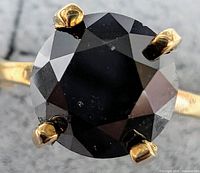 Top-down macro view of round black diamond in six-prong 10K yellow gold setting