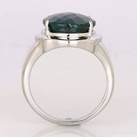 Side view showing the ring's full silver band with platinum plating and the oval dyed emerald secured by four prongs.