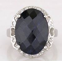 Close-up top view of ring showing large faceted oval dyed sapphire center stone and surrounding white topaz.