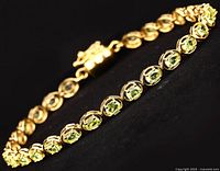 Bracelet laid out showing the yellow gold plating and the oval peridot stones along the full length.
