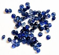 Top-down image showing a scattered pile of small loose round faceted blue sapphire gemstones on a white background.