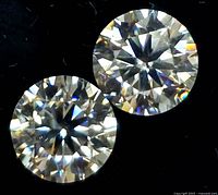 Close-up of two round moissanite stones showing cut and clarity on dark background.