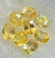 Nine oval faceted yellow sapphires placed on a white fabric background, showing various angles and facets to highlight clarity and color.