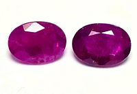 Close-up photo of two oval-shaped faceted ruby gemstones showing their red and purplish hues and polished facets.