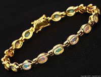 Close-up top view of the oval opal stones set in yellow gold plated links of the bracelet on black background.
