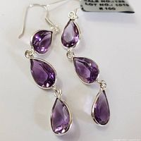 Close-up photo of a pair of silver earrings each set with three faceted pear-shaped amethyst stones in descending size from top to bottom on silver hooks.