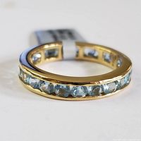 Close-up image of a sterling silver ring set with multiple blue topaz gemstones around the band, showing the faceted stones and polished finish.