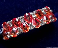 Close-up view of the row of pear-shaped orange sapphires set in silver prongs on the ring band showing color and cut detail.