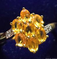Close-up photo showing the top of silver ring with oval yellow sapphire cluster and prong settings.