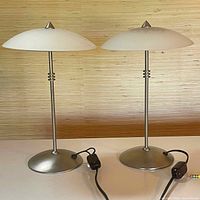 Two matching table lamps with metal stems and frosted glass dome shades shown side by side.