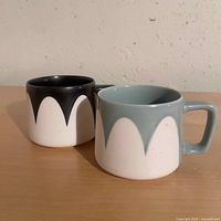 Two Starbucks mugs side by side, showing black and light blue interiors with white scalloped exteriors.