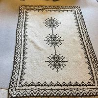Cream-colored area rug with black geometric central motifs and border on carpeted floor.