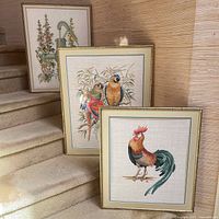 Three framed needlepoint artworks displayed on staircase, showing overall lot contents and details of framing and subject matter.